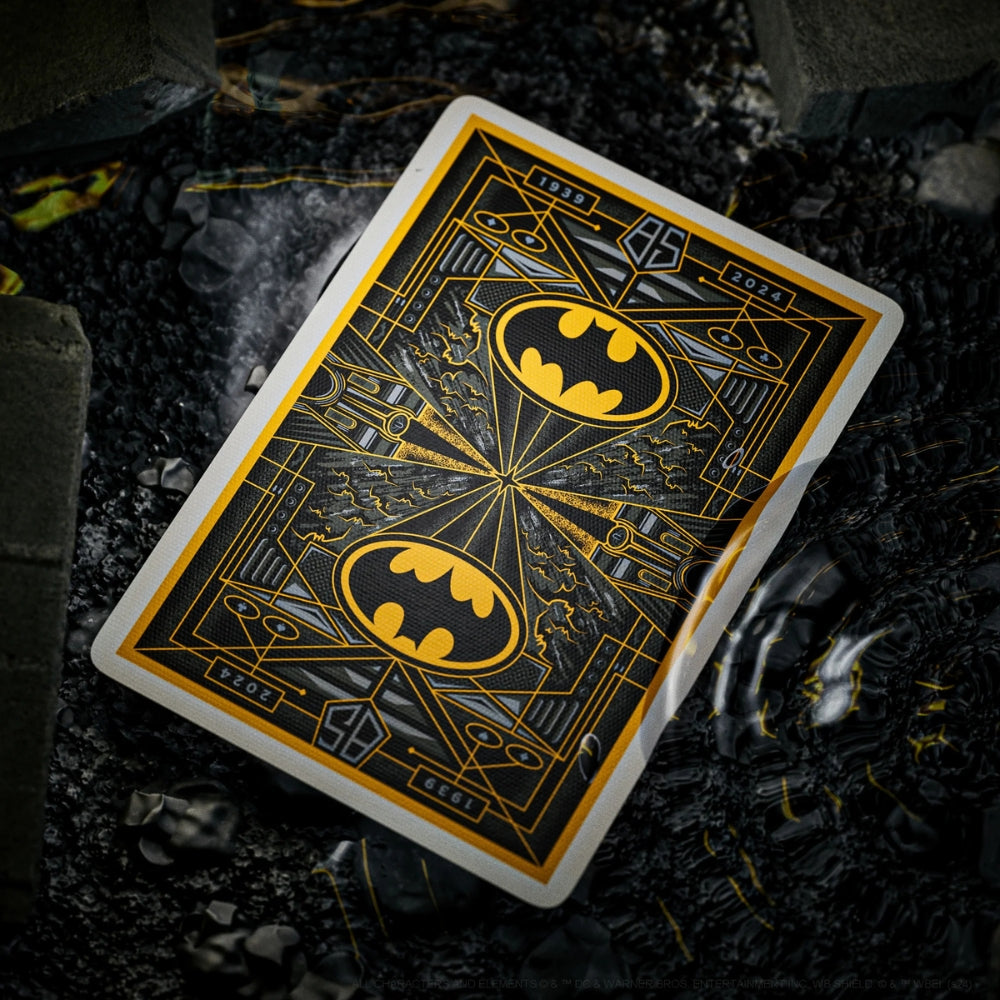 Back of a batman playing cards, laying face down in a puddle of water on some black stone