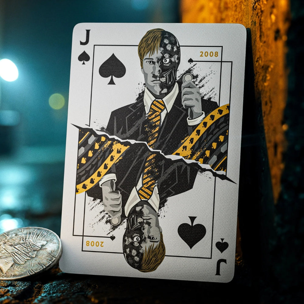 Jack of spades taken from a set of batman playing cards, leaning against a stone wall, but a damaged coin next to it