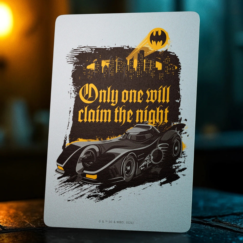 An extra card taken from a set of batman playing cards. It has a picture of the bat-mobile in the forefront, and the bat symbol shining out of a city in the background. There is also the text - Only one will claim the night