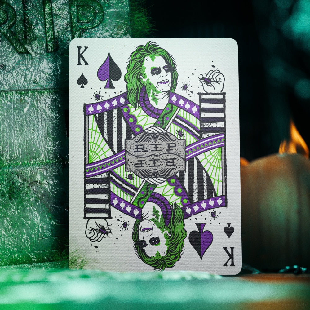 King of spades card, from a deck of Beetlejuice playing cards, leaning against a tombstone, with RIP on it.