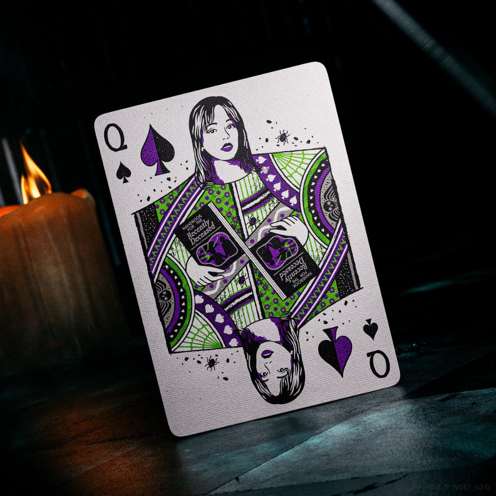 Queen of spades from a deck of Beetlejuice playing cards, in a dark creepy setting with a candle burning in the background