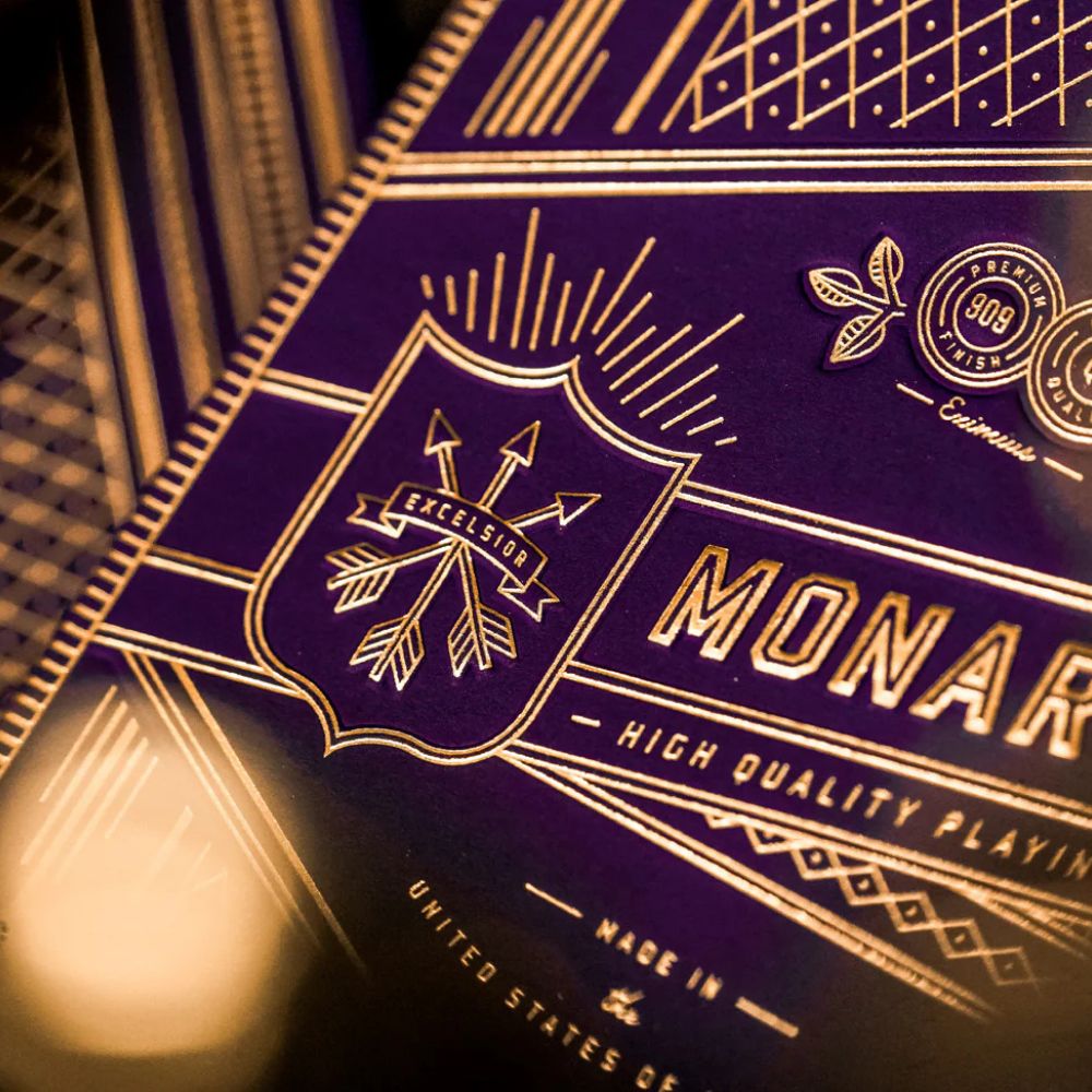 Super close up picture of the detail on a deck box of purple monarch playing cards - a sash with 3 arrows and the text Excelsior are featured
