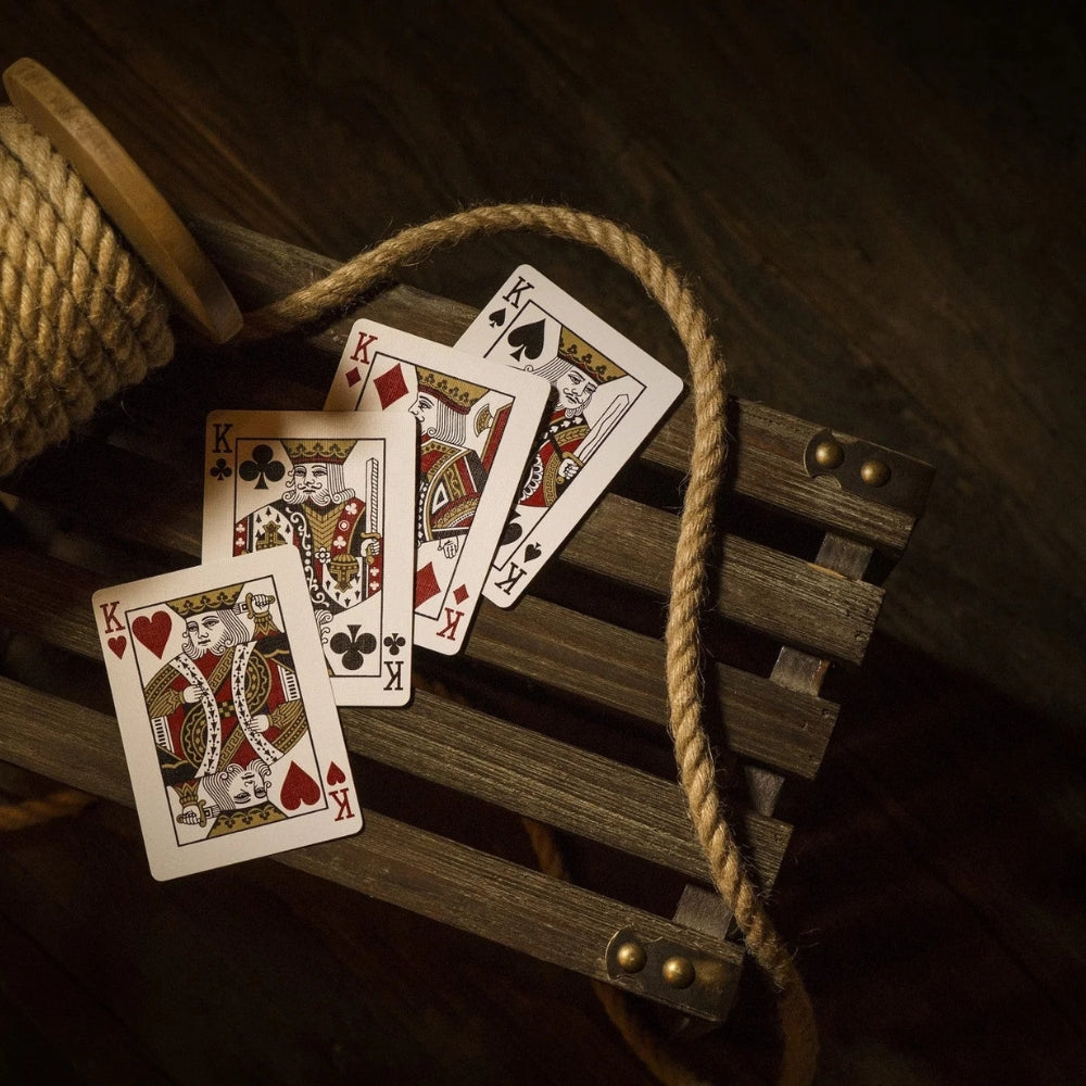 4 kings from a set of red monarch playing cards, laying on a wooded slated box, with some rope or twine around them