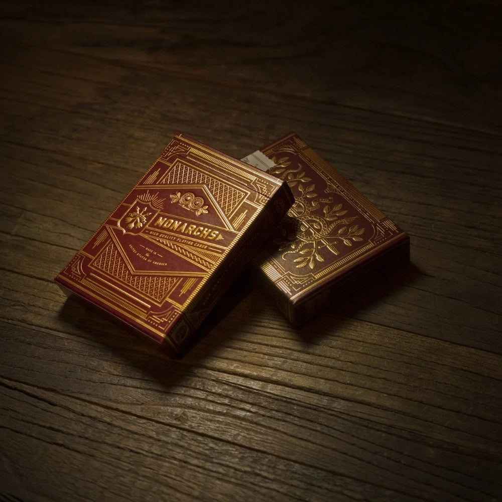 Two decks of red Monarch playing cards laying over each other at an angle, both on a solid wooden desk