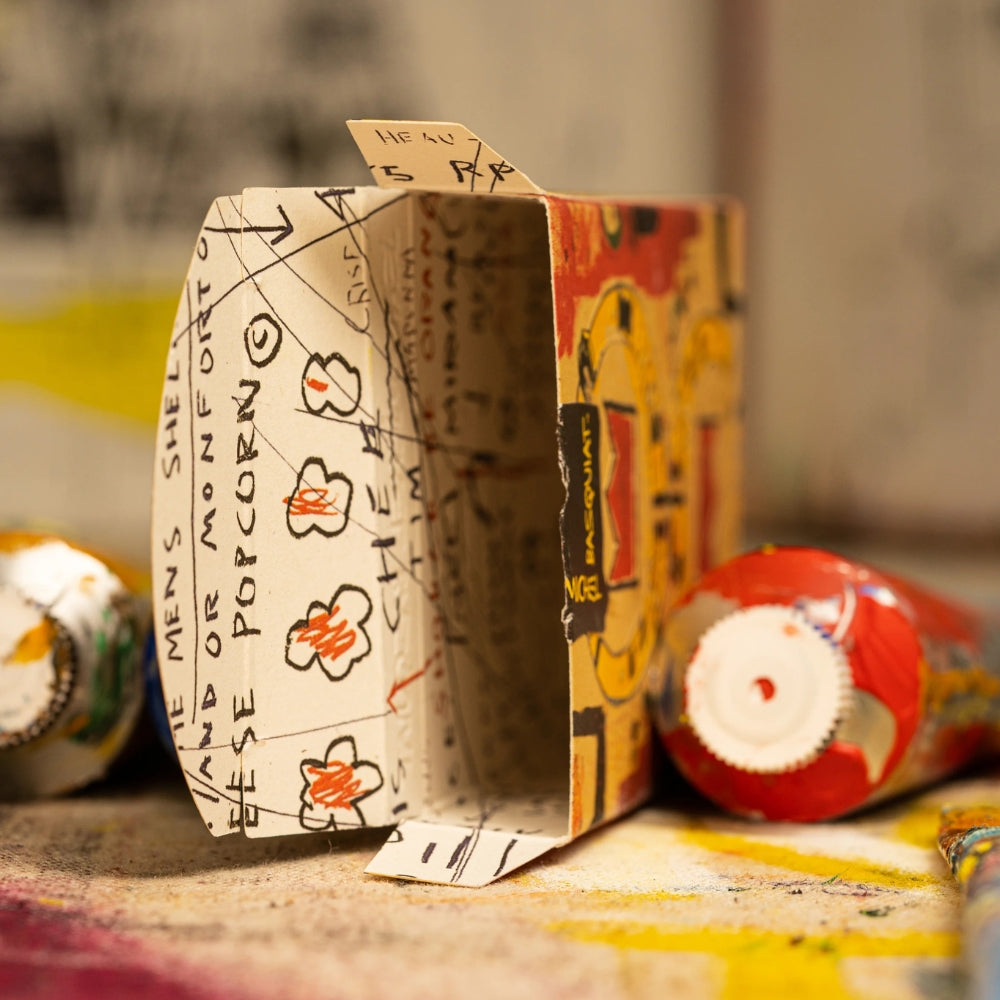 inside of a deck box of basquiat playing cards, with a tube of paint either side