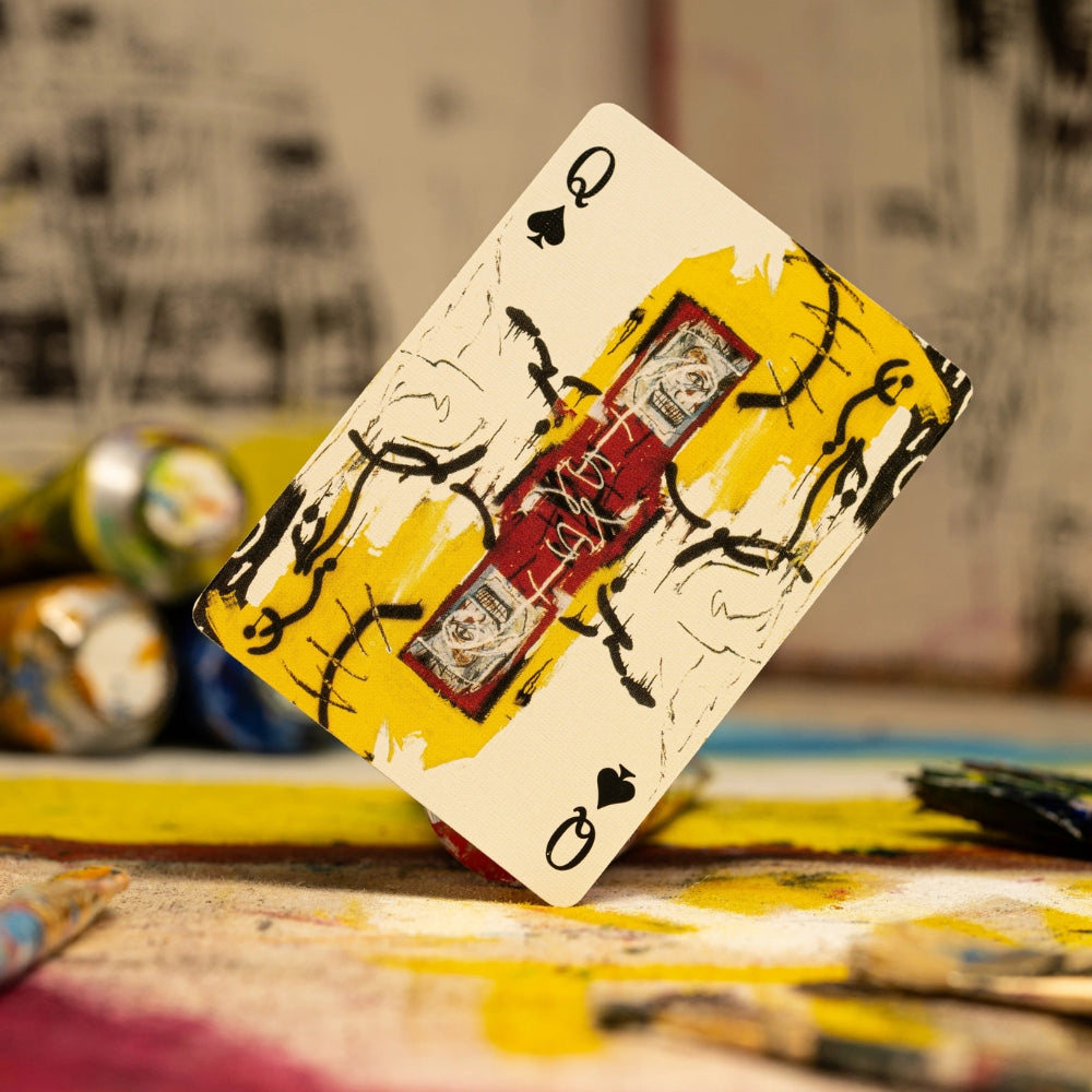 Queen of spades from a deck of basquiat playing cards, surrounded by art materials