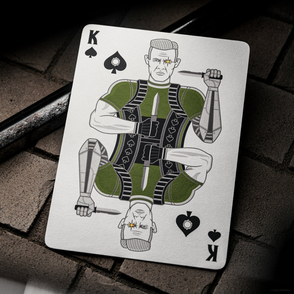 King of spades from a set of deadpool playing cards, laying on a brick surface with a metal bar in the background