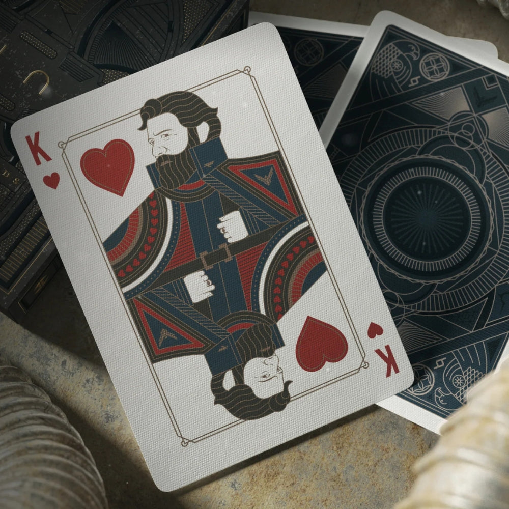 Picture of the king of hearts spread over some other cards and the deck box on a sandy surface