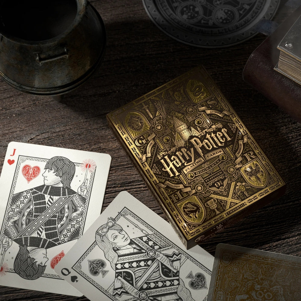 Picture of the Hufflepuff Harry potter deck box and two face cards on an old wooden desk, also features a books and other items on the desk