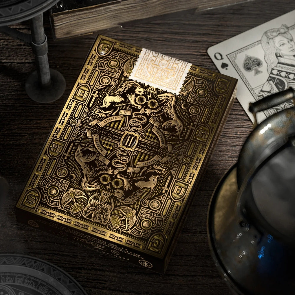 Close up of the back of the Hufflepuff deck box, with the queen of spades sitting in the background, all on a wooden desk.