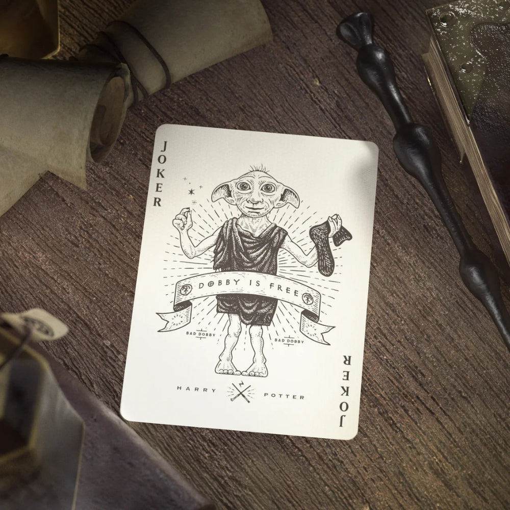 Joker card (Dobby is free) sitting on a wooden desk with parchments and a wand surrounding the card.