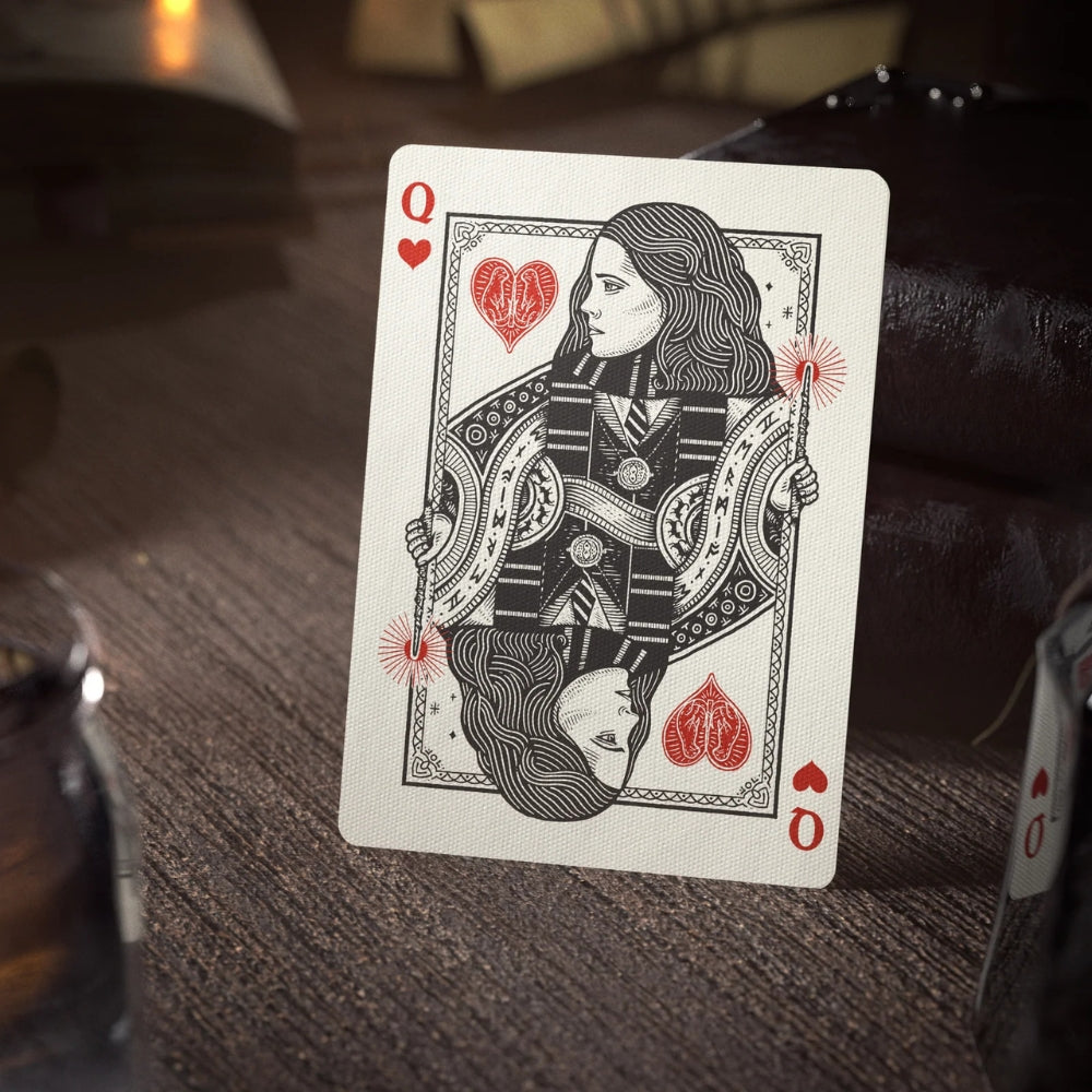 queen of hearts card leaning against two leather bound books on a wooden desk.