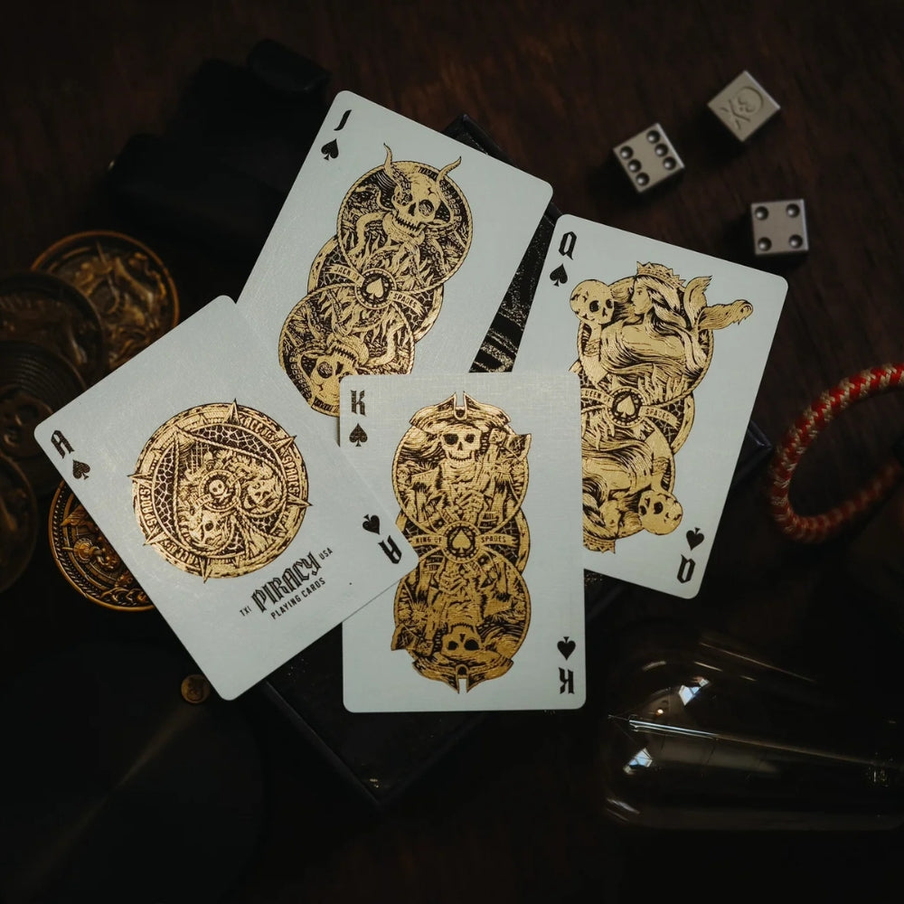 Jack, Queen, King and ace of spades from piracy playing cards deck, also features some metal dice and metal coins - all laying on a wooden desk