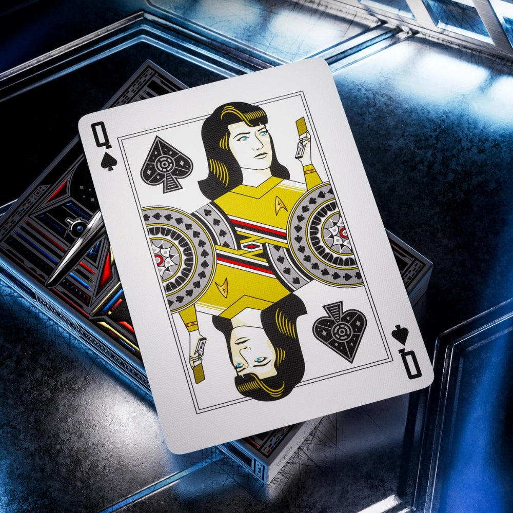 Queen of spades playing card, laying on a deck box, which is laying on a metal surface. The card is featured in a deck of star trek playing cards