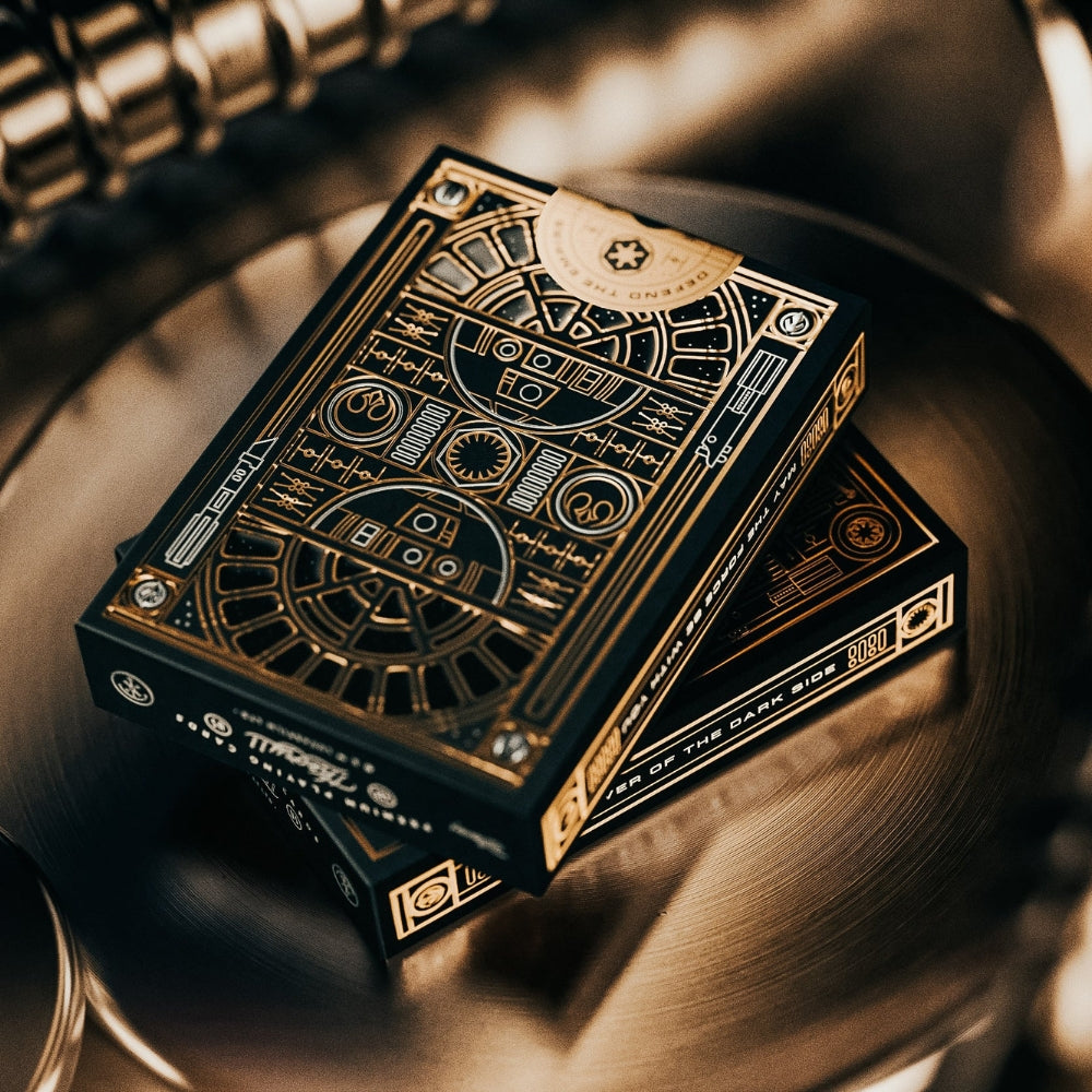 two black and gold star wars playing card deck boxes sitting on a round metallic surface