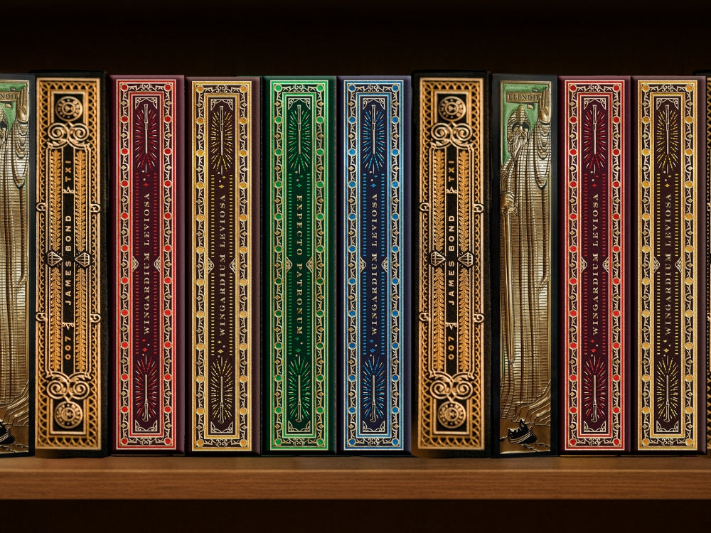 A row of premium playing cards designed to look like ornate book spines on a wooden shelf, visually representing the idea of books featuring playing cards.