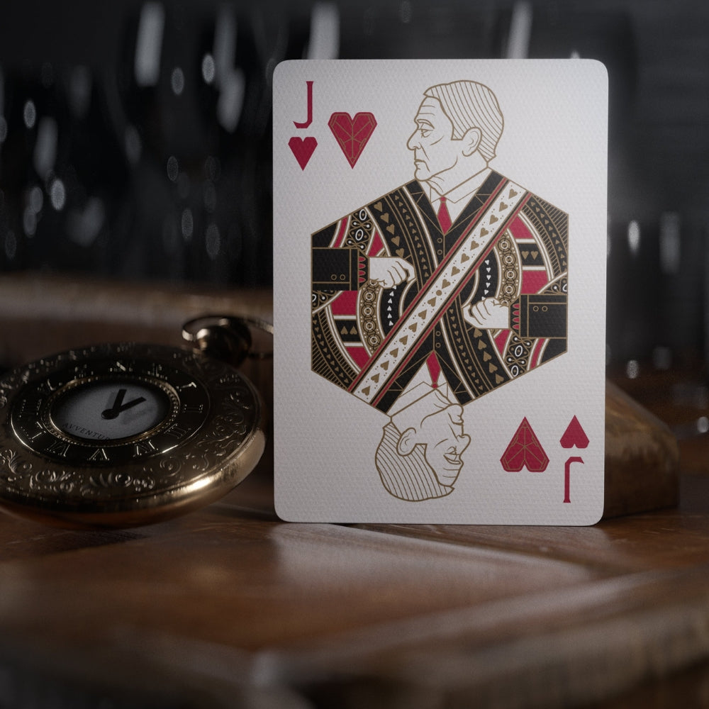 Jack of hearts playing card, standing upright on a wooden desk, with a pocket watch laying next to it.