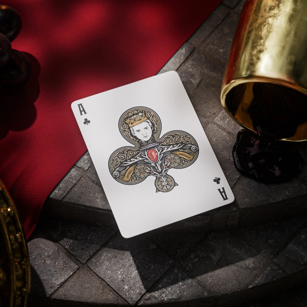 Ace of clubs card from a set of game of thrones playing cards, laying on a stone surface, with a gold goblet and some grapes nearby