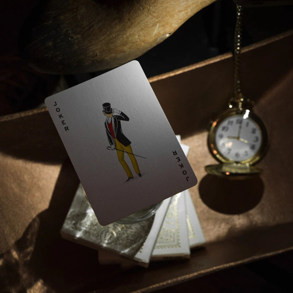 Joker card taken from a set of ivory tycoon playing cards.  The deck is floating over 3 decks of cards and a pocket watch can be seen in the background