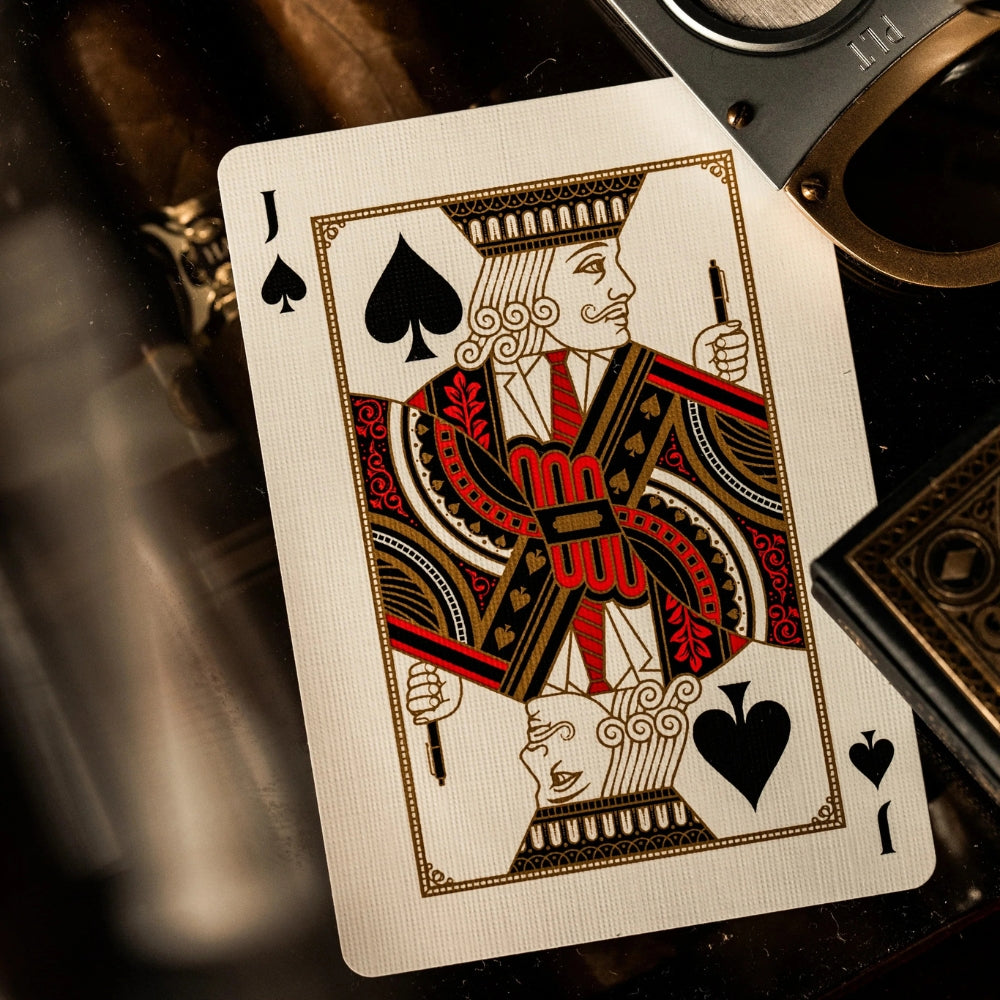 Jack of spades from a James bond playing cards set, also partially in shot are a bottle of drink, deck box and cigar cutter.