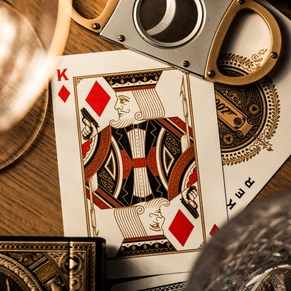 King of diamonds playing card, layout over a joker card.  Surrounded by a cigar cutter, two drinks glasses and a deck box (all partially in the shot)