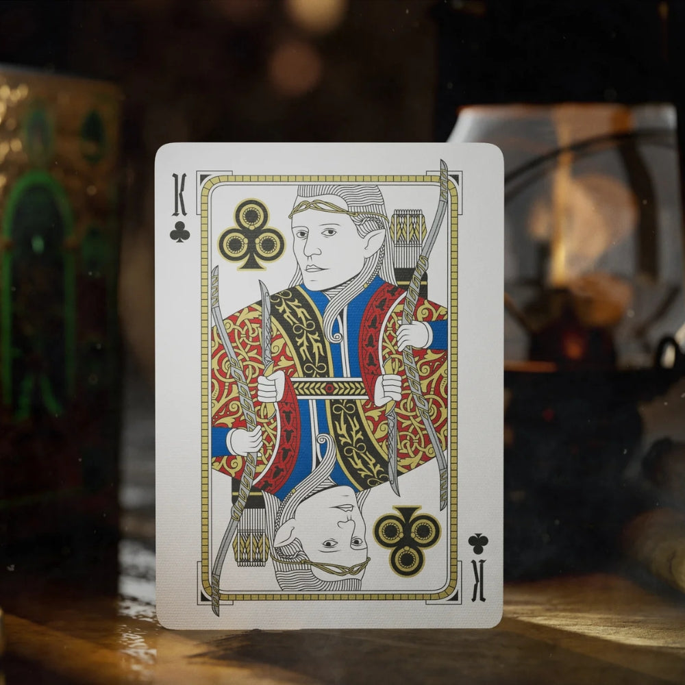 King of clubs playing card, standing on a wooden surface with a deck box and lantern in the background
